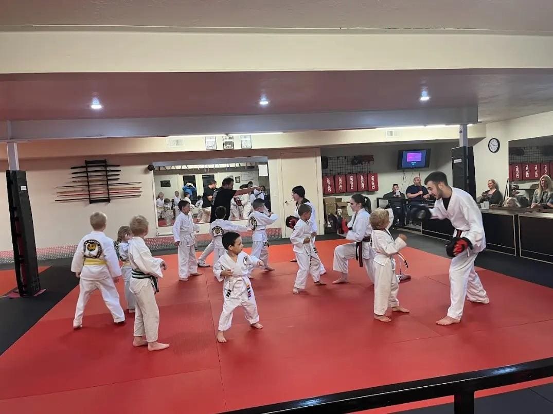 Children performing coordinated jiu jitsu kata movements with wooden training weapons during class
