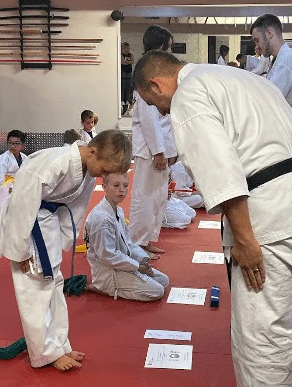 Children bowing to instructor during a jiu jitsu belt promotion ceremony inside a martial arts dojo